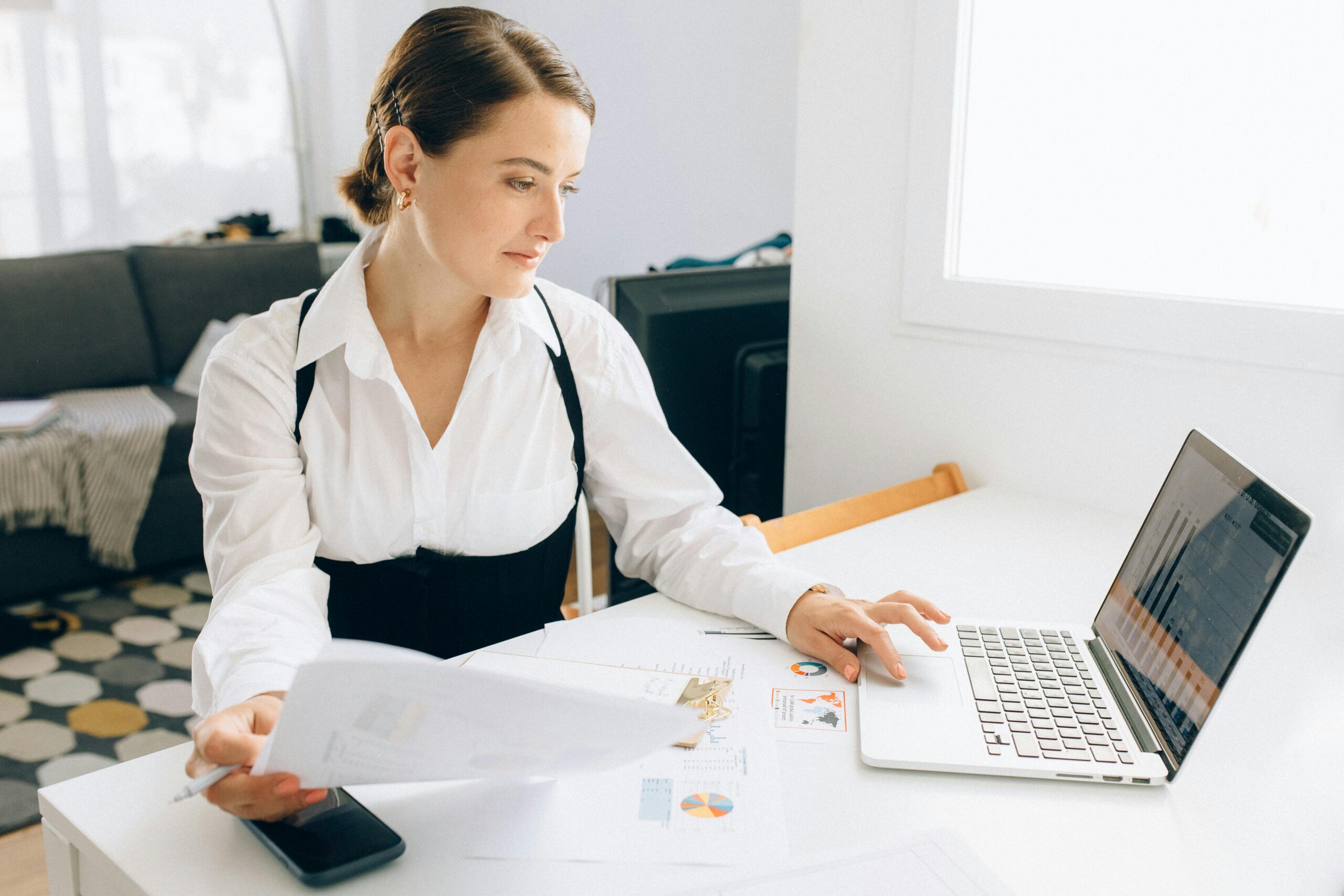 woman sitting at desk typing on a laptop and holding a sheet of paper