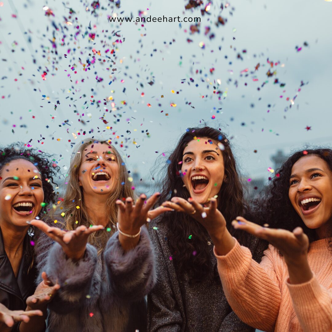 Image shows 4 women laughing and throwing confetti in the air