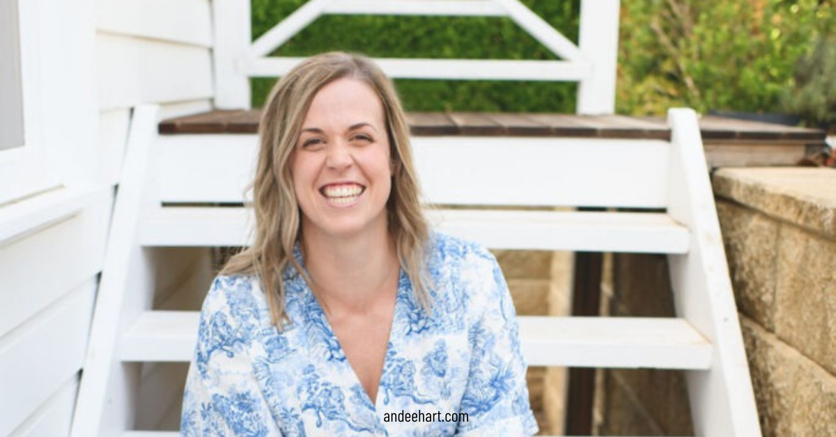 Image is SJ Meeson who is a guest on the She Sells Differently Podcast and she is smiling at the camera while sitting on some white stairs