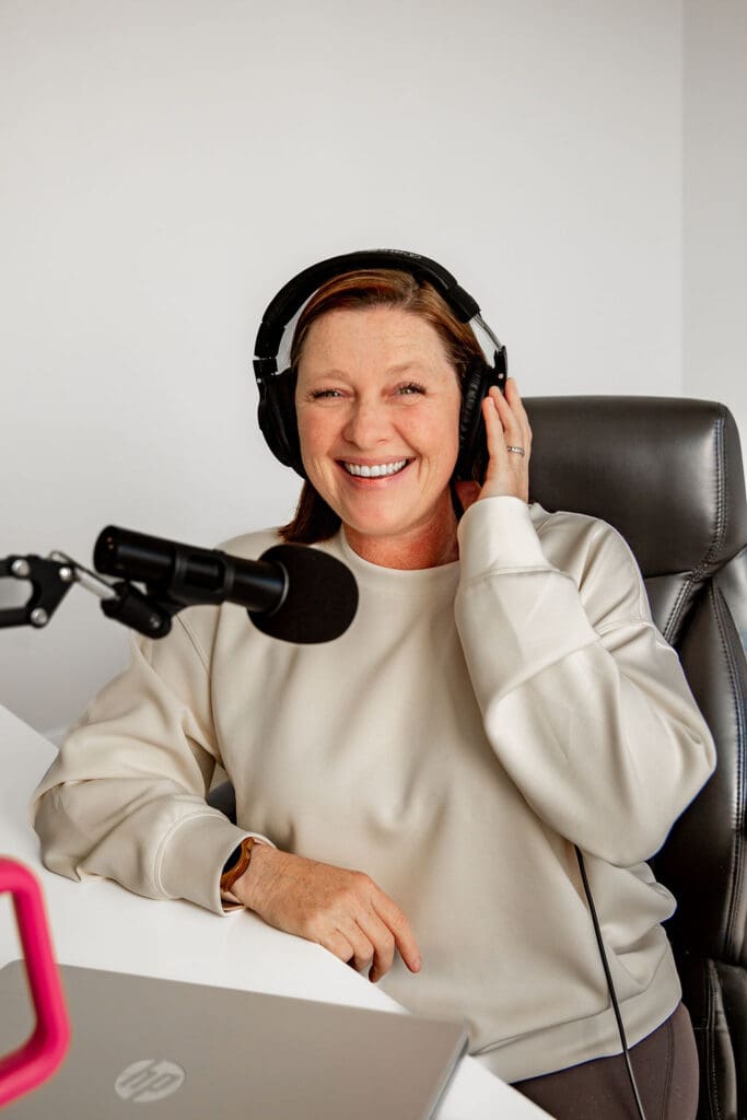 Image is of Liz Chapman, podcast manager, and guest on the She Sells Differently podcast, she is smiling at the camera with headphones on and a microphone near her mouth